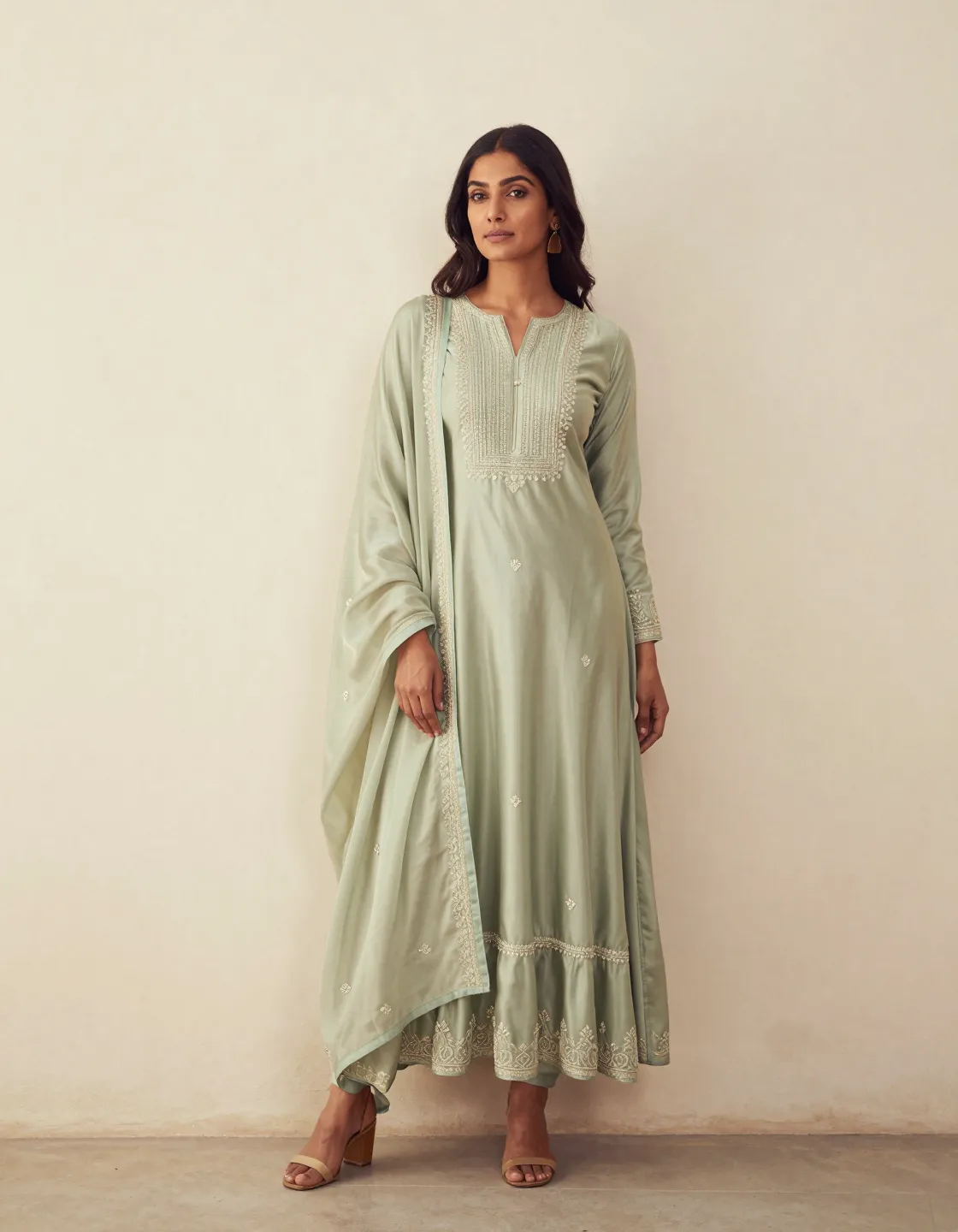 A model in a sage silk anarkali against a limewashed wall